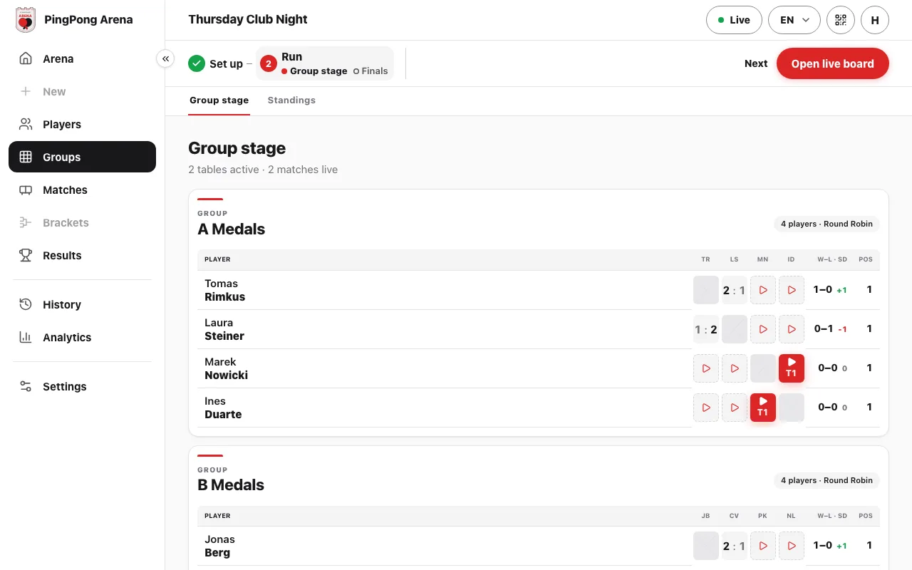 Group tables with finished scores, red live tiles marked T1 and play icons for matches still to come