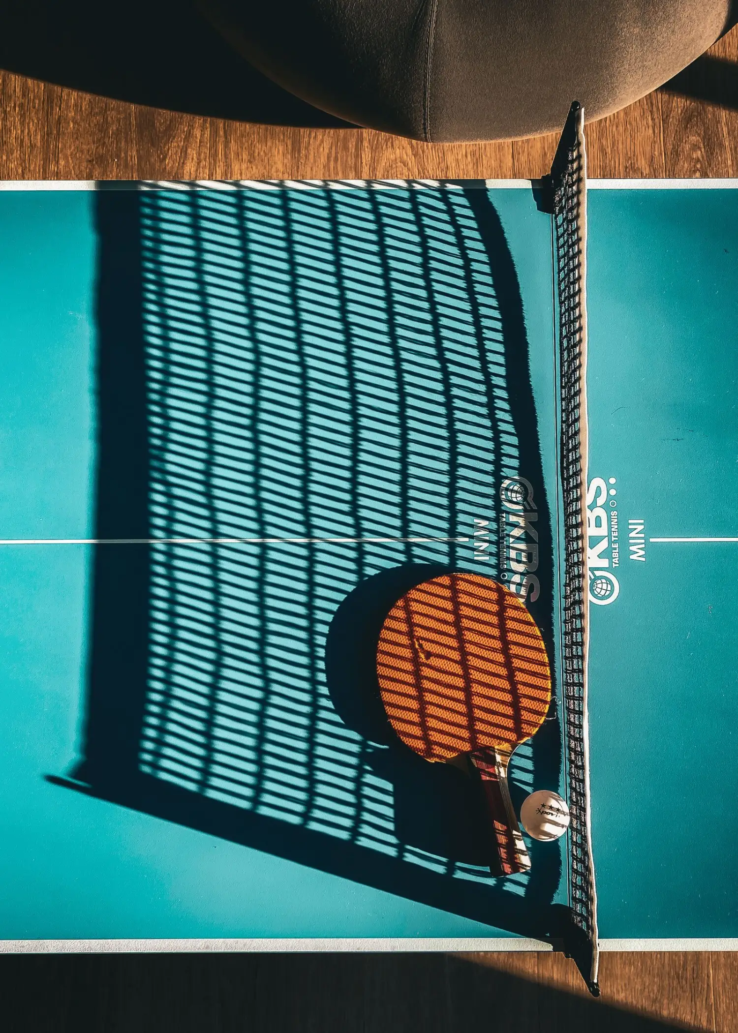A table tennis bat and the long shadow of the net across the table