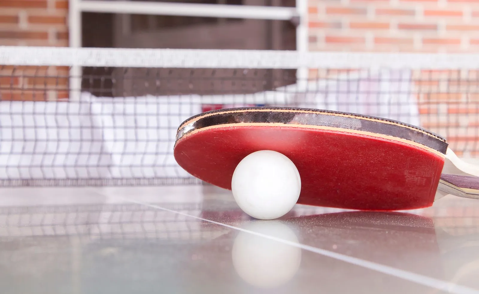 A red table tennis bat resting on a ball against the net