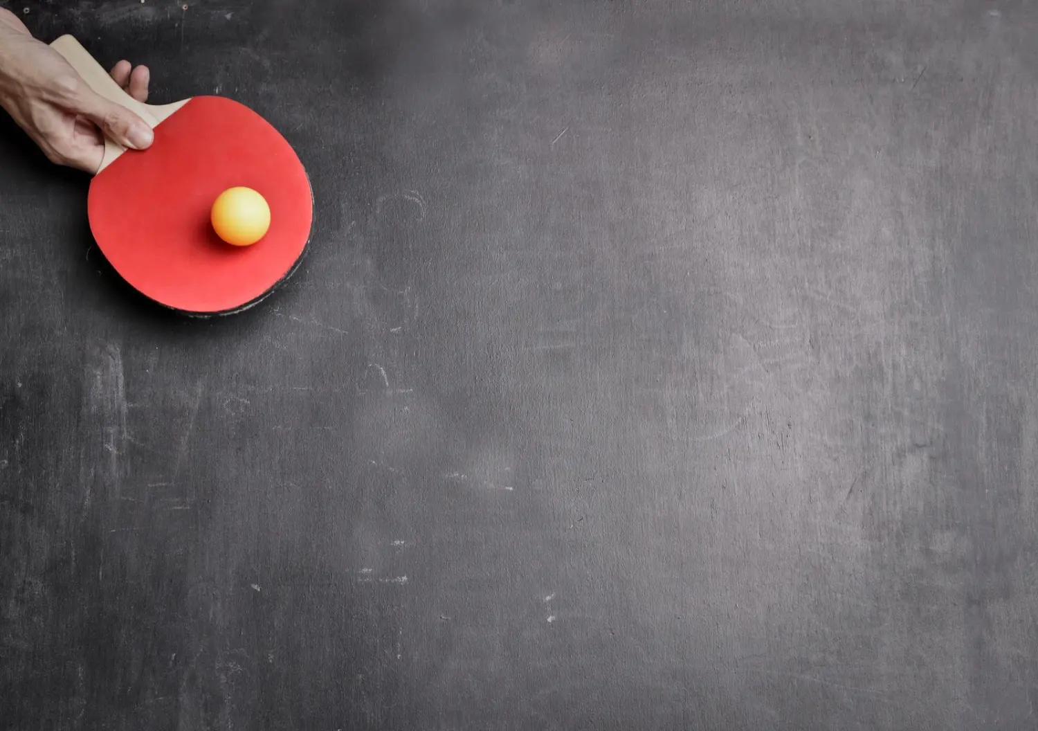 A hand holding a red table tennis bat with a ball